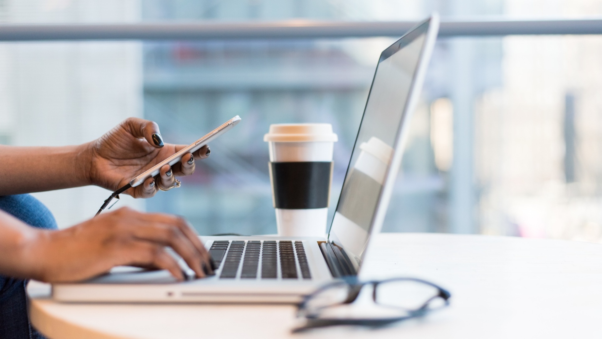 Woman's hands show holding a cell phone while working on a laptop