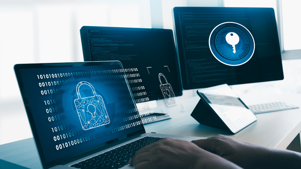 A desk with two computers displaying a padlock and key on the screens