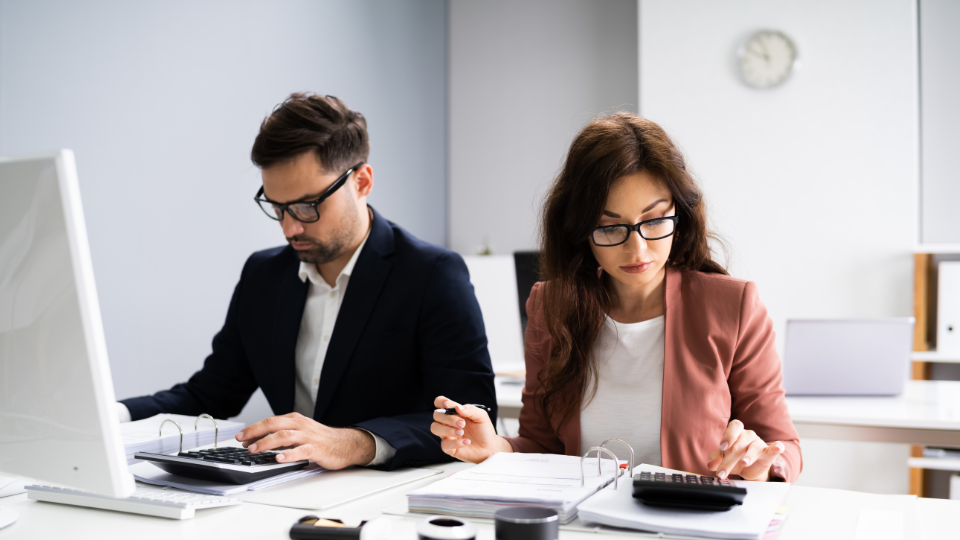 Two people working at a desk in front of a computer