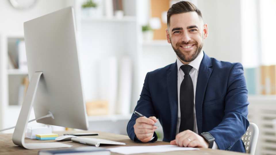 A businessman in a suit sitting at a desk with a computer on it