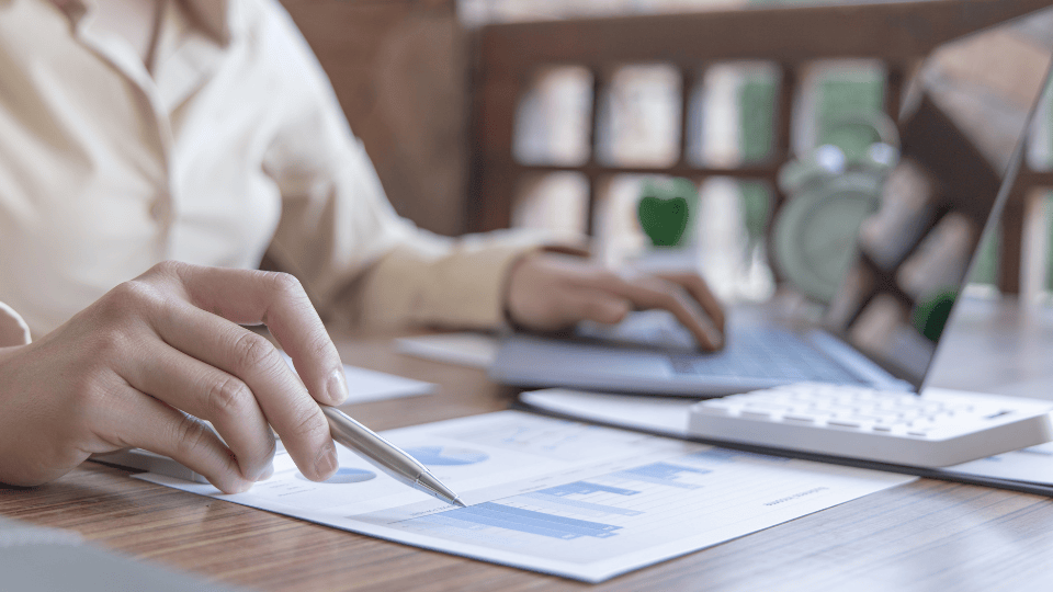 A person sitting at a table with a laptop looking at a document with metrics on it