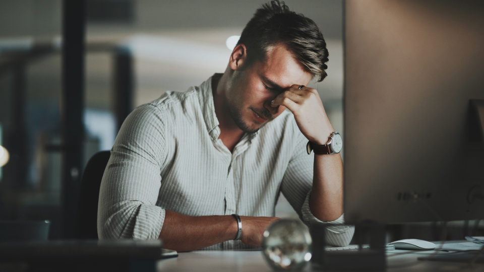 A person sitting at a desk in front of a computer with a hand on his head with a stressed-out expression to symbolize legal billing challenges