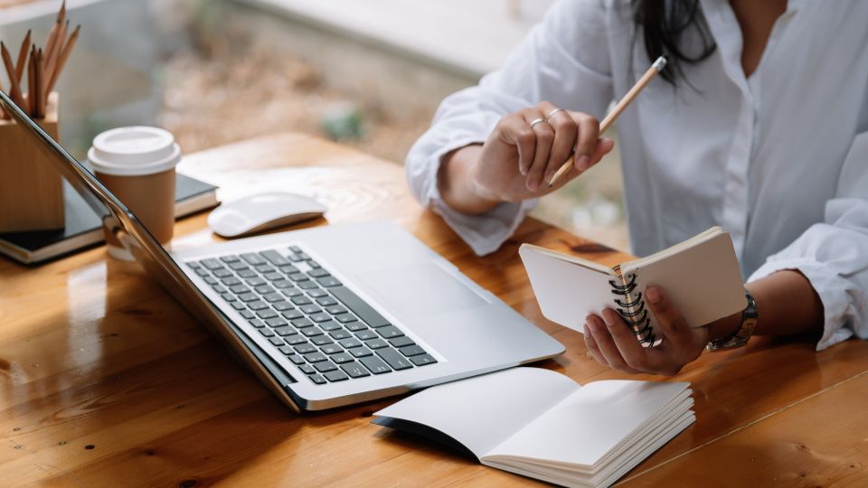 A person working on a laptop at a desk with a notebook and a cup of coffee.