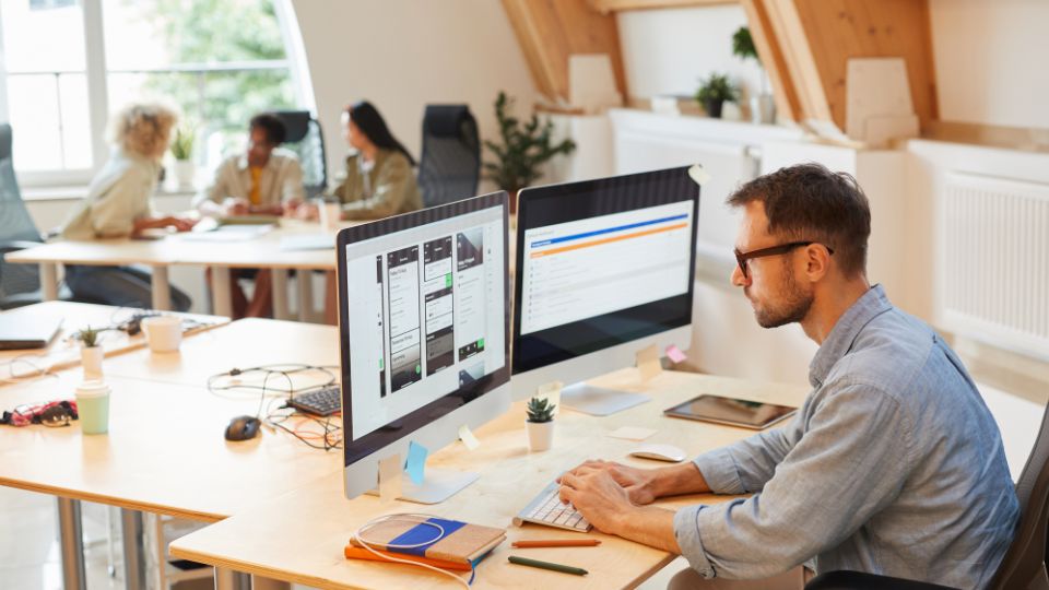 A person is sitting in front of two computers in an office.