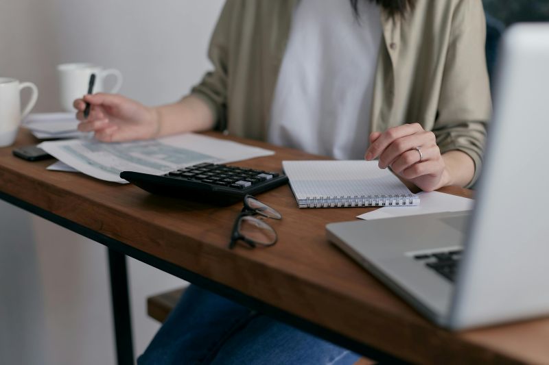 A person works at their desk with a laptop, pen, and notebook on the table