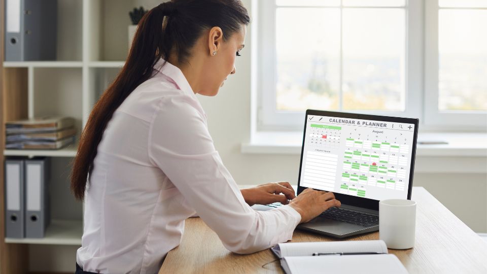 A professional sitting at a desk with their laptop open and a calendar displayed.