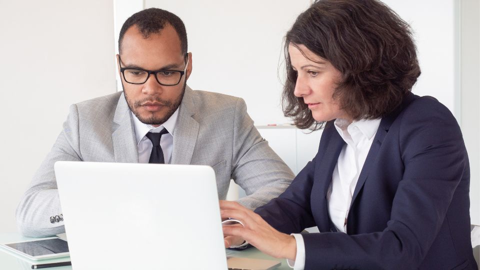 A legal professional with their laptop open on a table while a colleague looks at the screen.