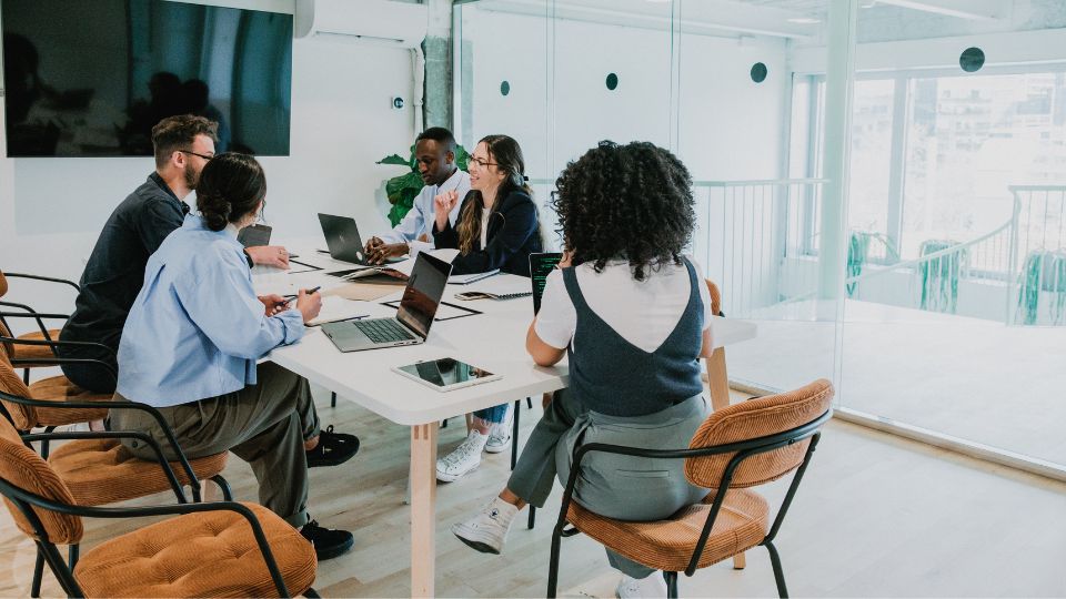 A group of colleagues sitting in a meeting room with laptops open on the table.