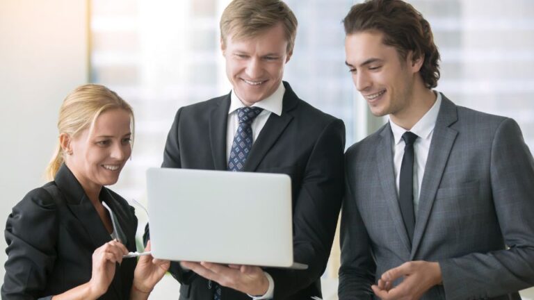 Three professionals looking at a laptop and smiling.