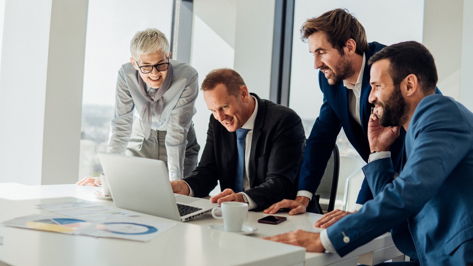 A group of professionals engaged in a discussion while looking at a laptop in a conference room