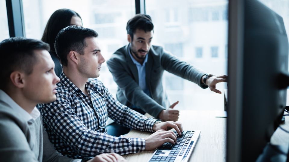 People in an office looking at a computer and collaborating.