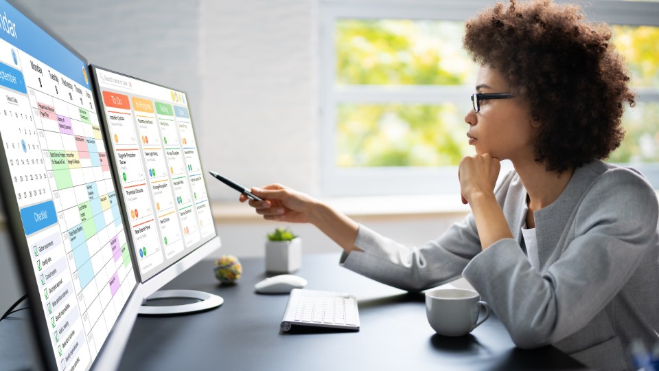 A professional working at a desk, checking a calendar and deadlines on two computer screens
