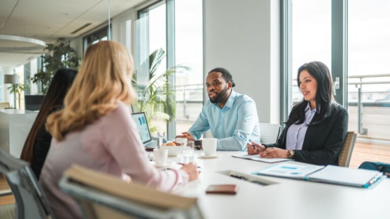 People sitting at a table in a conference room with various documents and a laptop on the table.