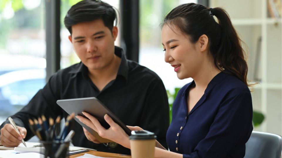 Two professionals in an office, looking at a tablet