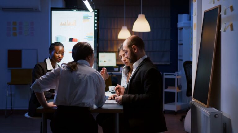 A group of colleagues at a meeting table actively analyzing computer displays in a corporate office