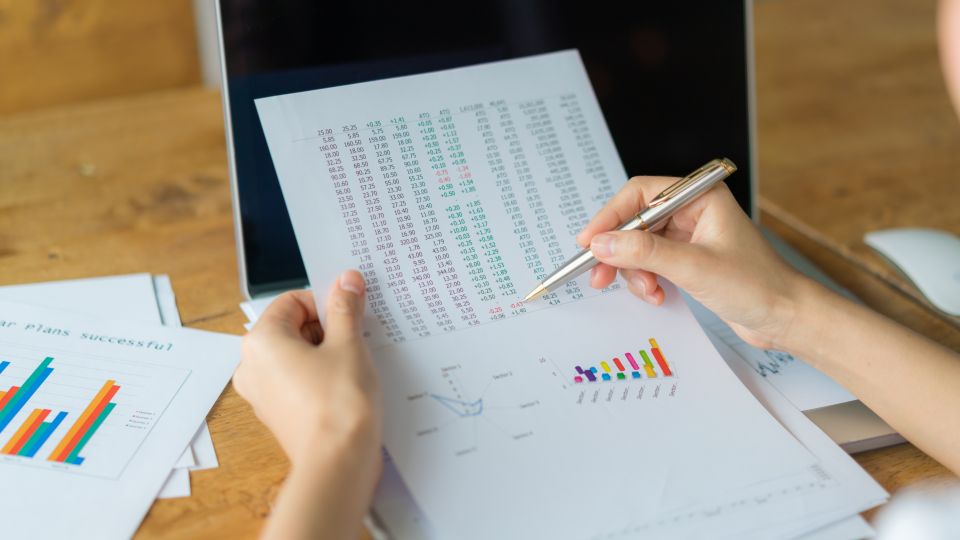 A person holding a financial report with columns of numbers in various colors, analyzing it with a pen