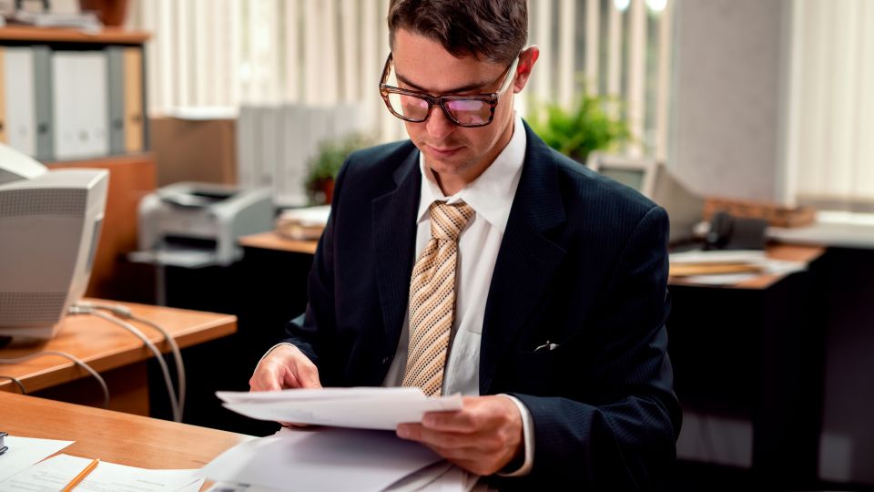 A business professional reviewing paperwork in an office, seated at a desk.