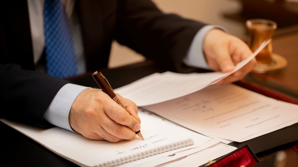 A close-up of a business professional writing in a notebook while holding other papers