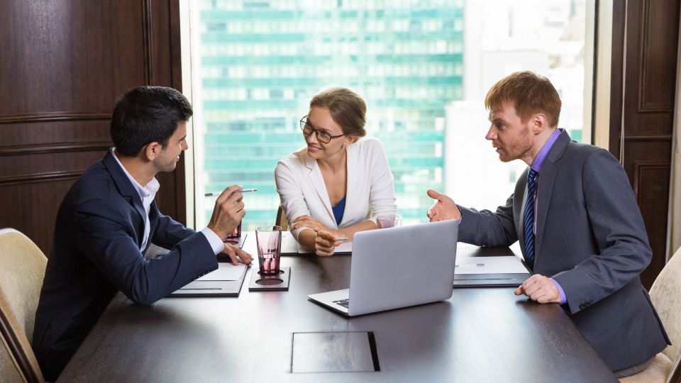 Three legal professionals engage in a strategic meeting around a laptop.