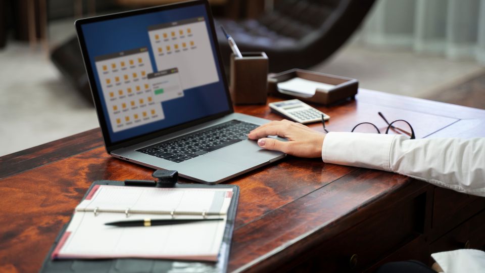 A close-up of a person's hand resting on the keyboard of a laptop that displays several folder icons on the screen.