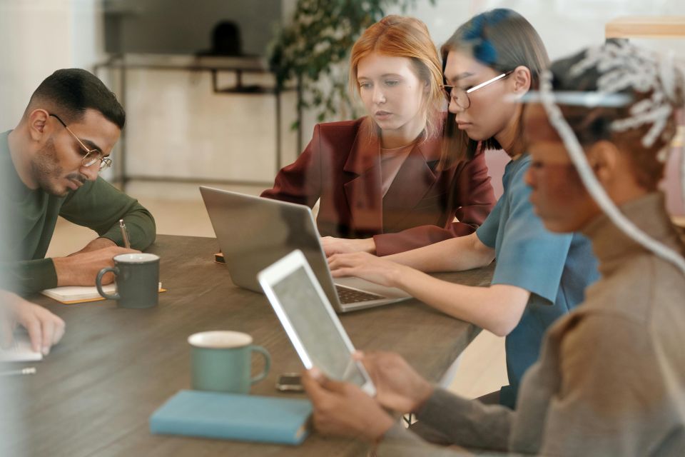 A group of people sitting around a table with laptops.
