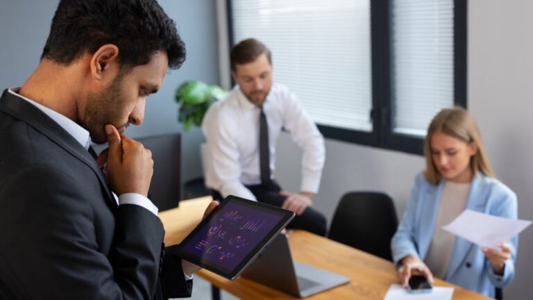 A man in a black suit looks down at a tablet displaying various graphs and charts.
