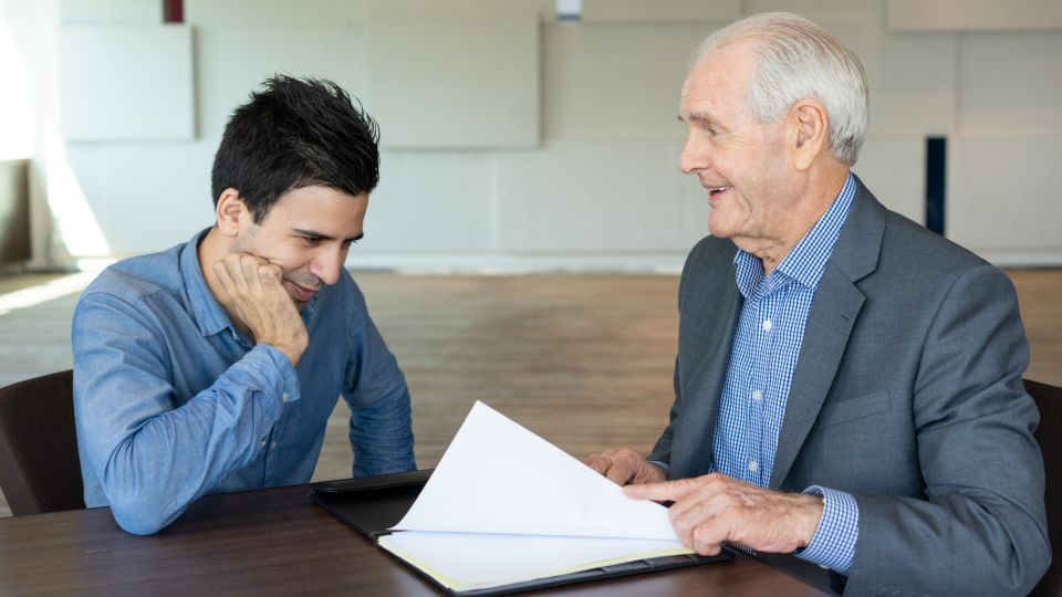 Two business professionals sit at a table and discuss a document