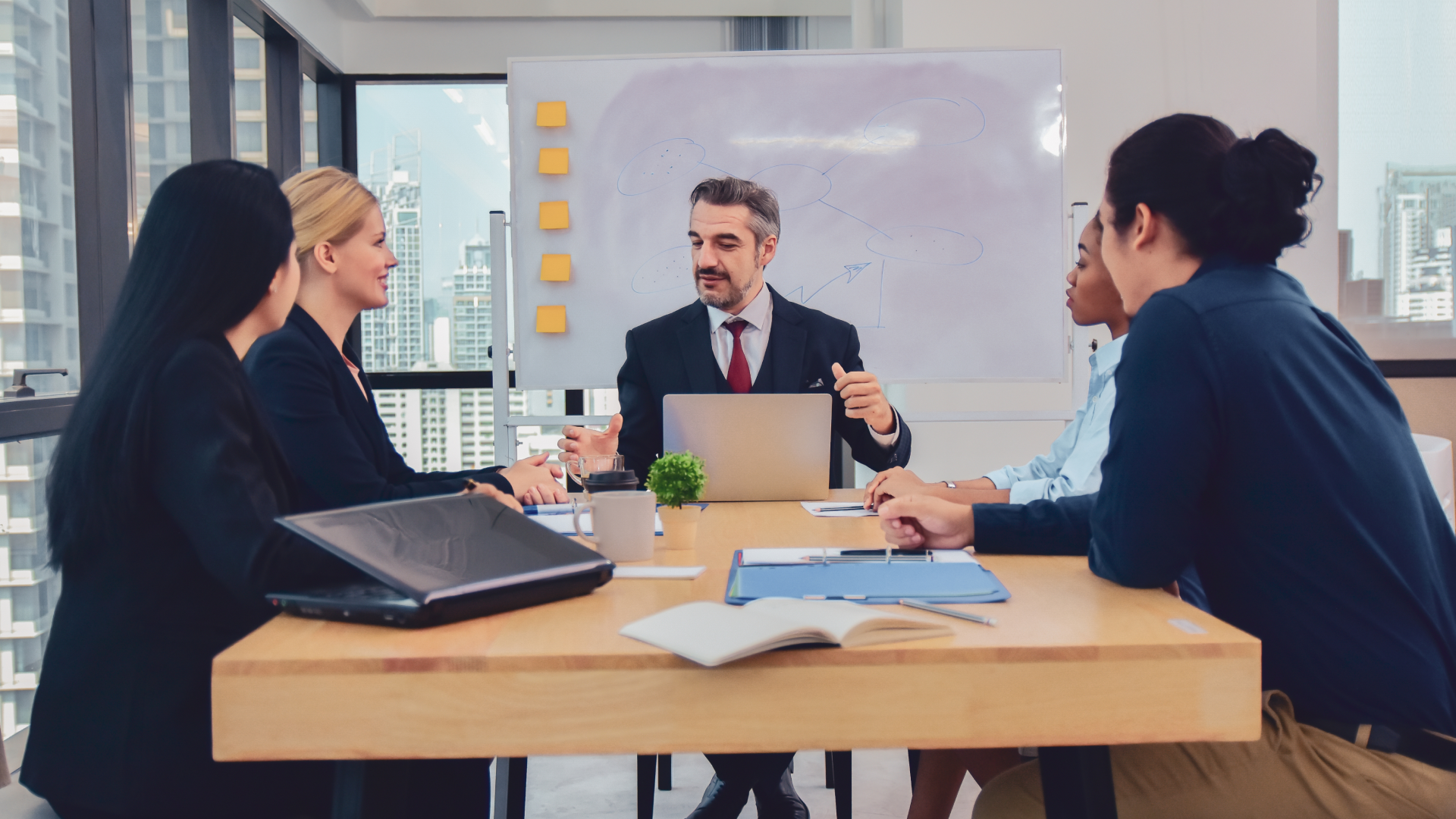 A man in a suit leads a meeting, gesturing with his hands while colleagues listen.
